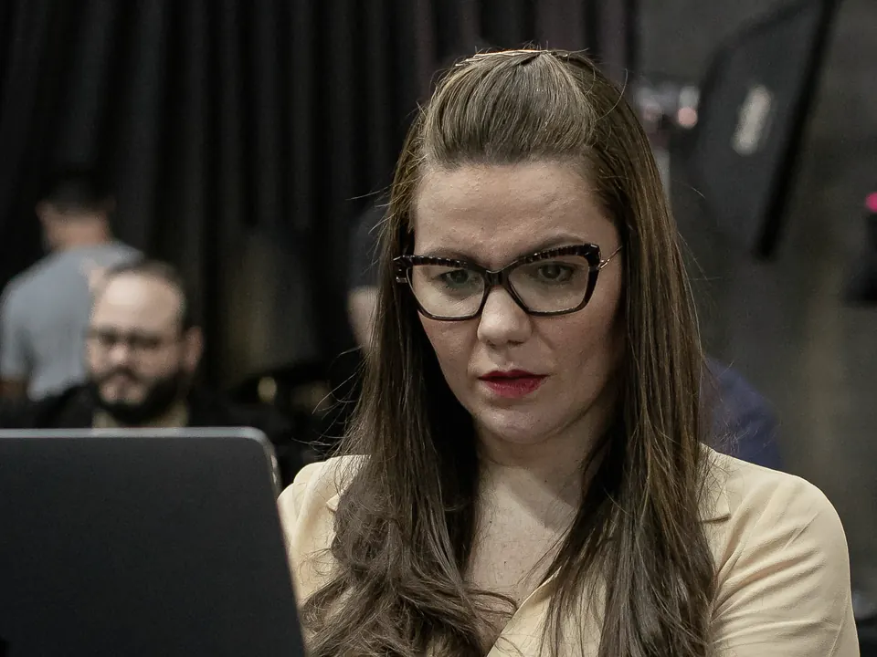 Nathália Gomes em um evento, diante do notebook, com pessoas ao fundo.