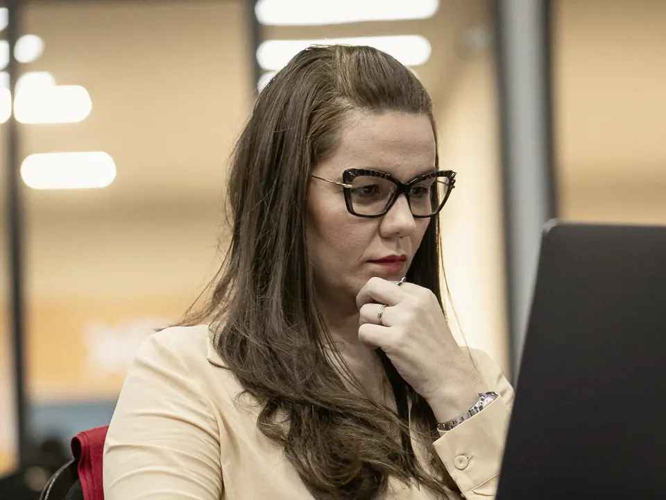Nathália Gomes diante do notebook, com a mão no queixo, em atitude de escuta.