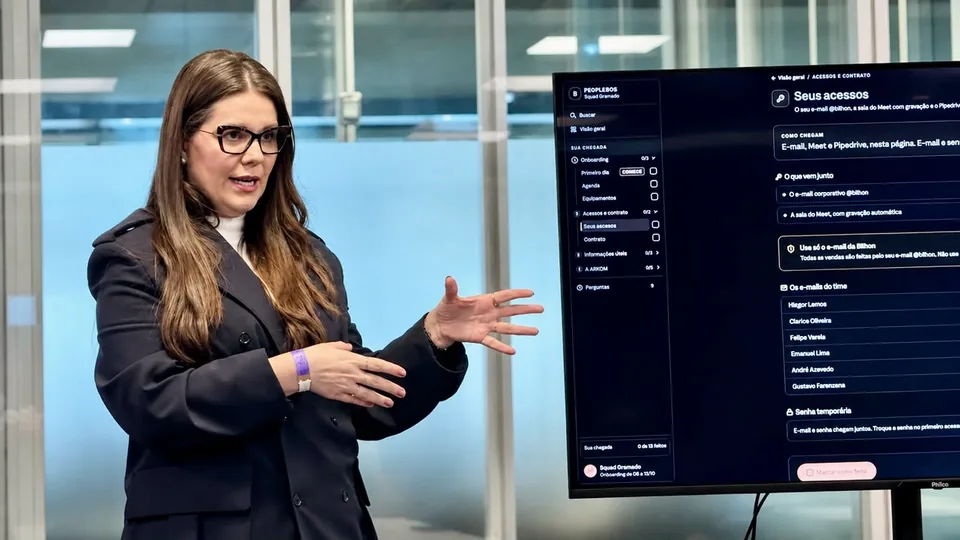 Nathália Gomes apresentando um sistema numa tela grande, numa sala de reunião.